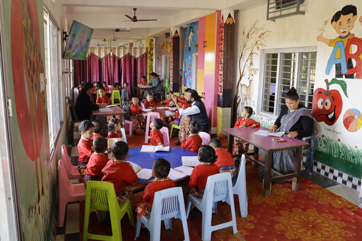 Nursery classroom — colourful walls, small tables, teachers with young learners